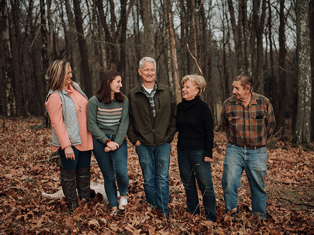 a multi-generational family smiling as they stand in a grove of trees on their land