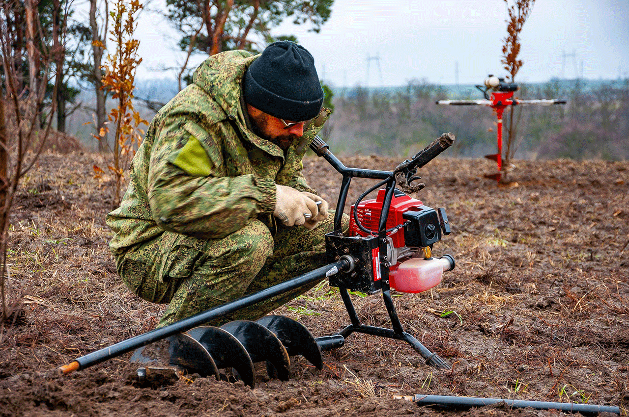 A forester crouches down to prepare a gas-powered auger to plant tree seedlings