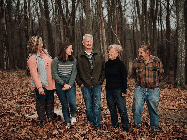 A multigenerational family smiling as they stand in a grove of trees on their land