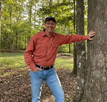 Consulting Forester Tom Manual leaning against the trunk of a tree Consulting Forester Tom Manual leaning against the trunk of a tree