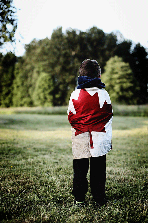 A boy draped in a Canadian flag gazes at trees
